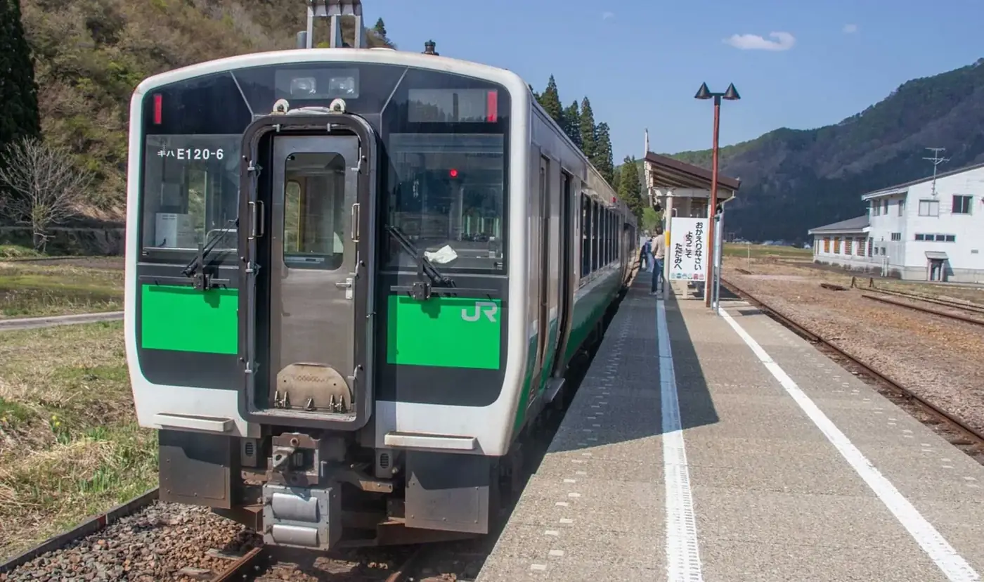 山あいの駅に停まる、緑の帯を巻いたローカル線の列車
