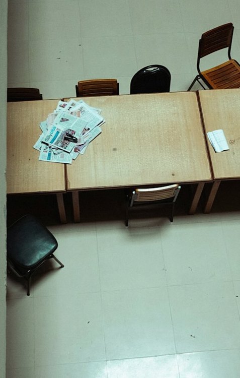 机と椅子が並ぶ殺風景な部屋で、机の上に書類が広げられている写真